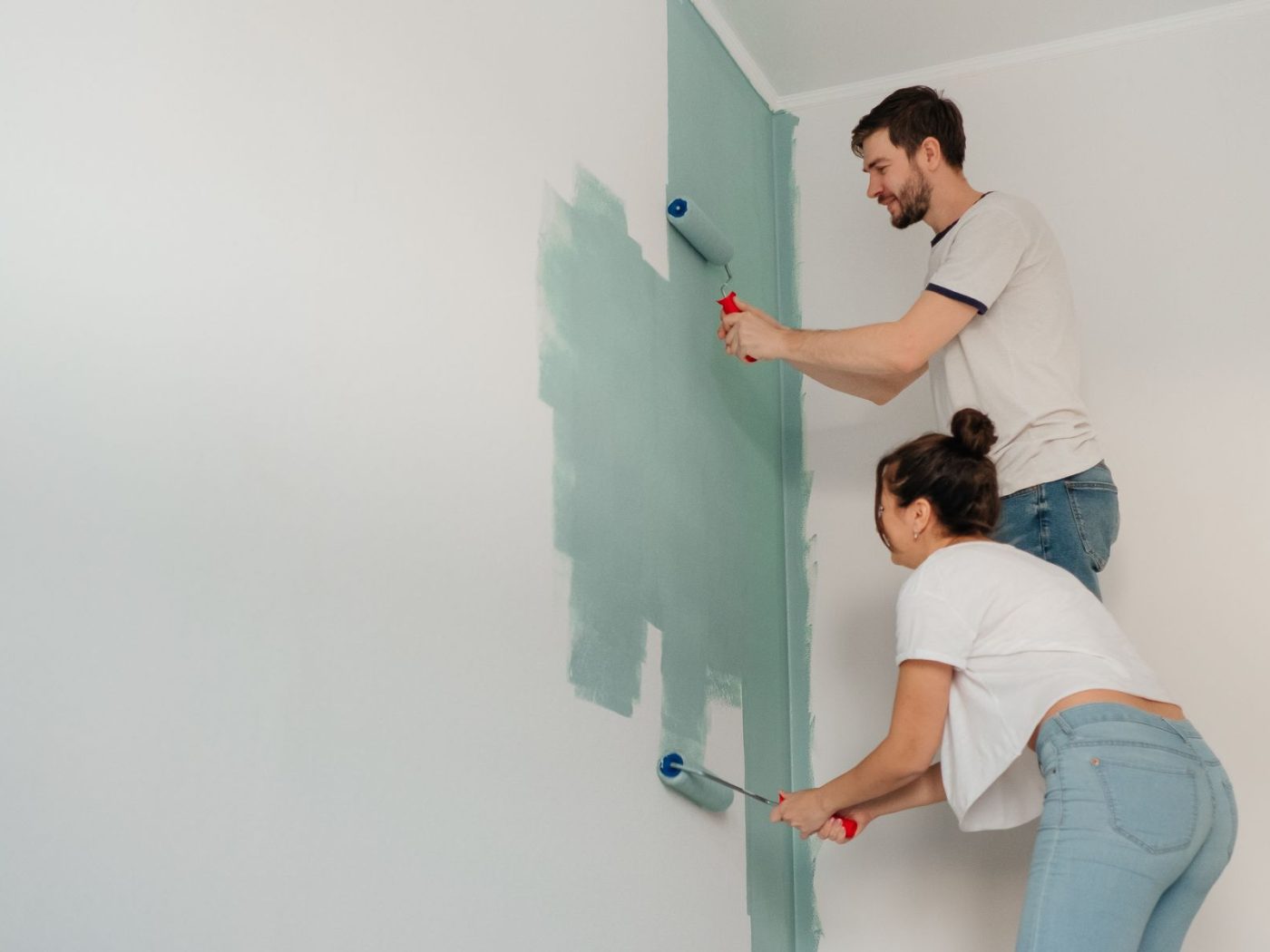Zwei Personen streichen gemeinsam eine Wand in Salbeigrün