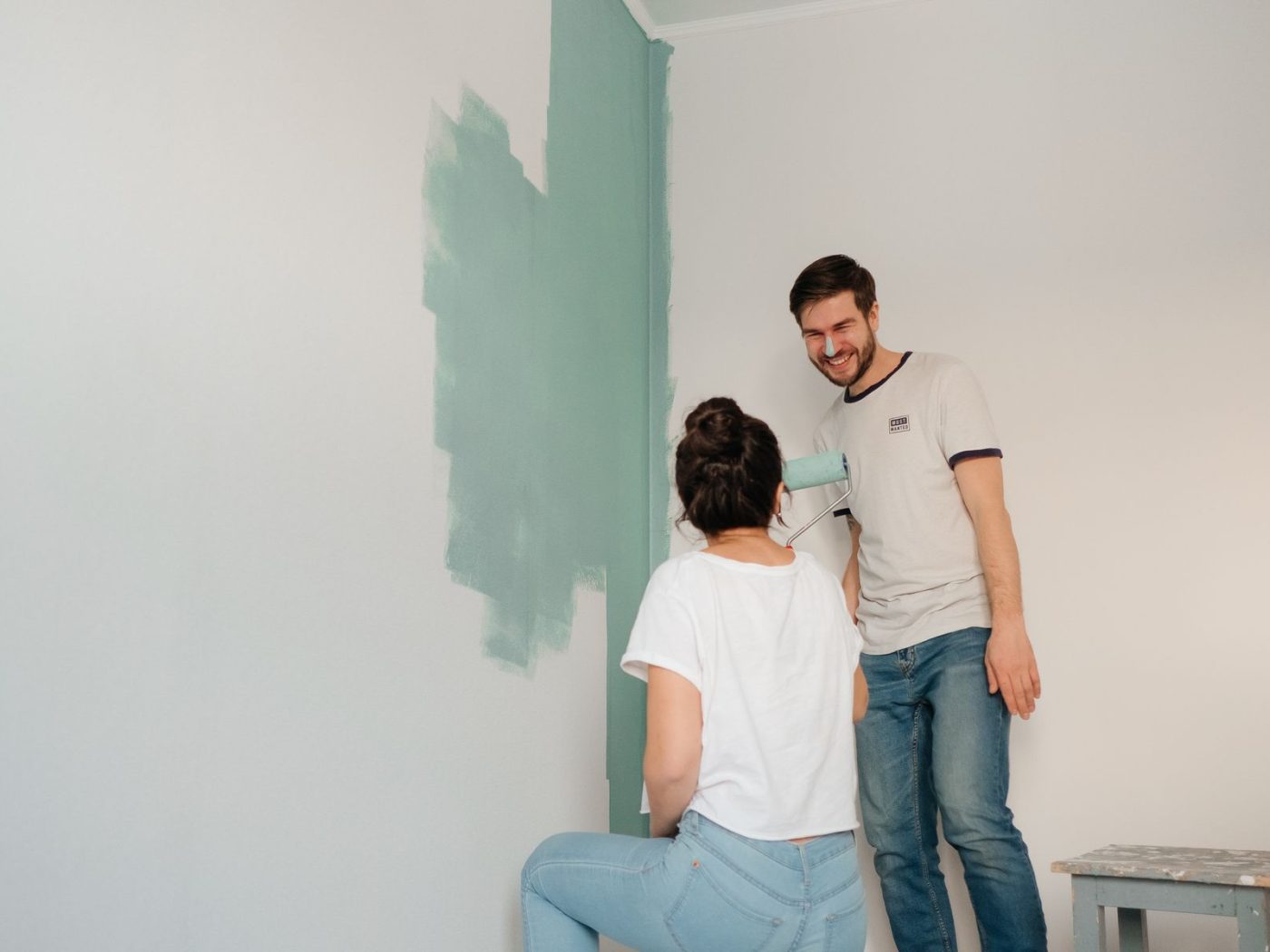 Paar streicht Wand in Salbeigrün mit Farbrolle